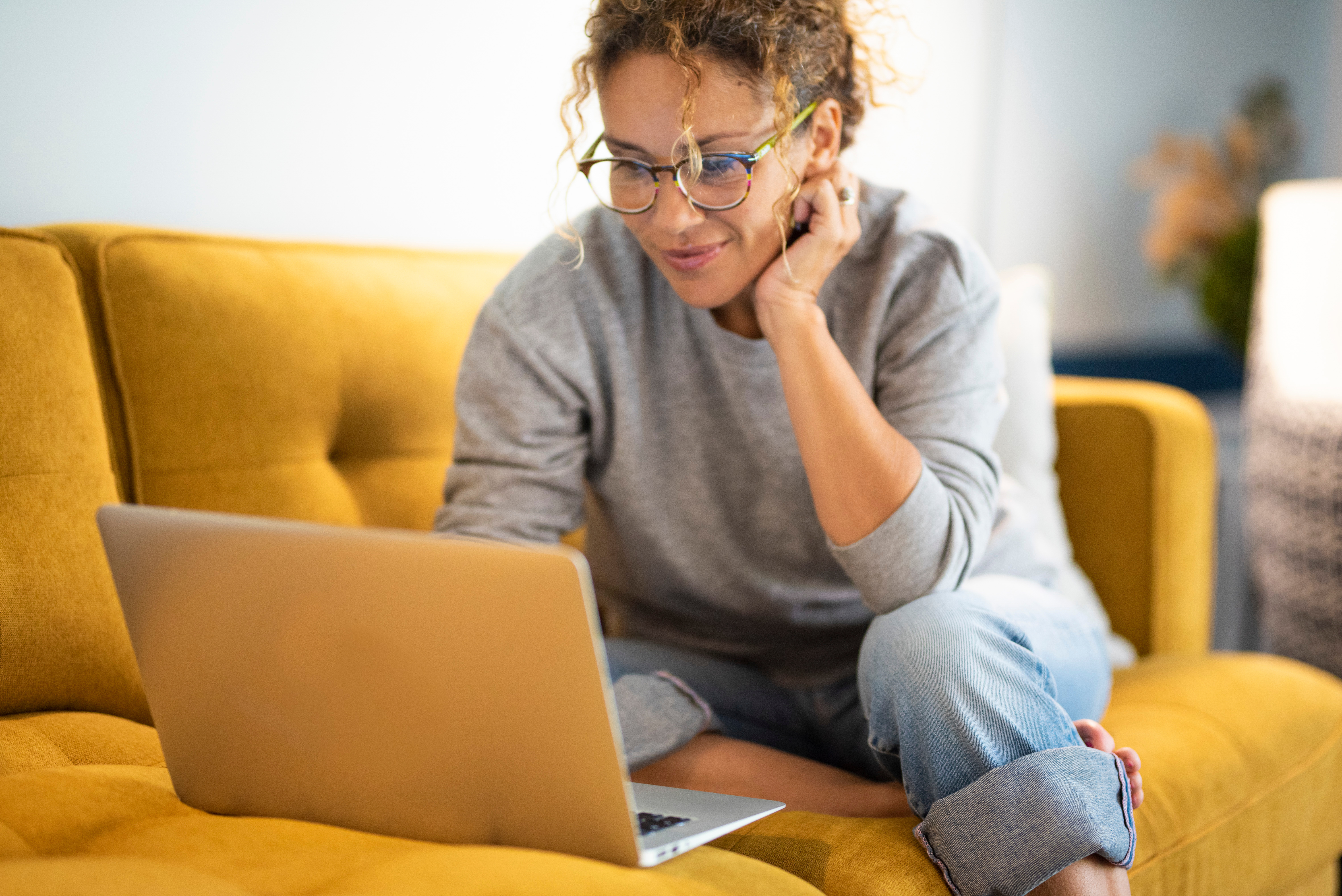 A woman checks her accounts on her laptop while sitting on a couch at home, confident that her finances are in order thanks to an unsecured personal loan from Telcoe Federal Credit Union.