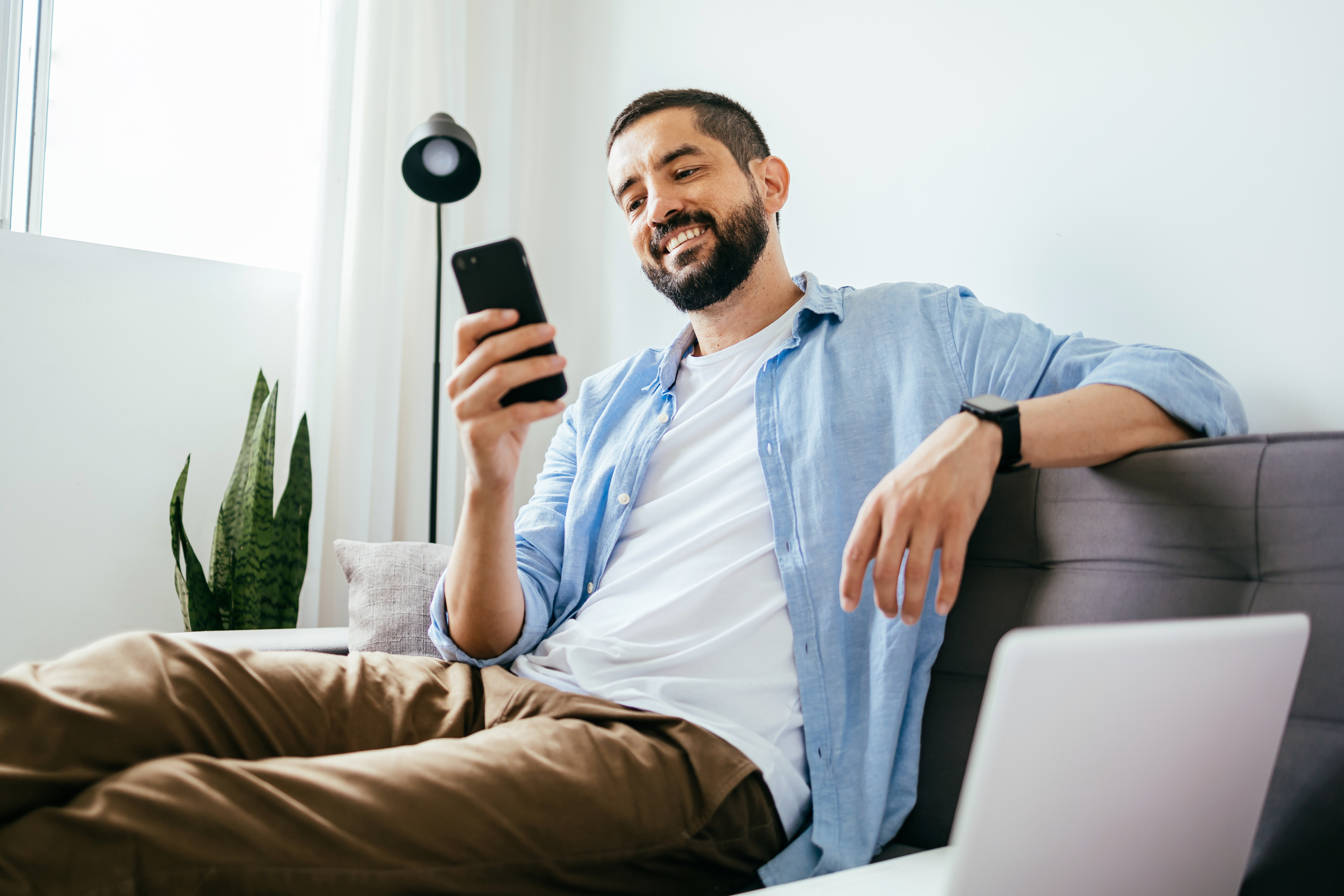 A man checks his phone while sitting on a couch at home